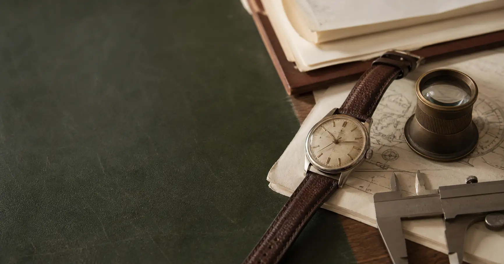 Illustrative unbranded mechanical watch, loupe, caliper, and research papers on a desk